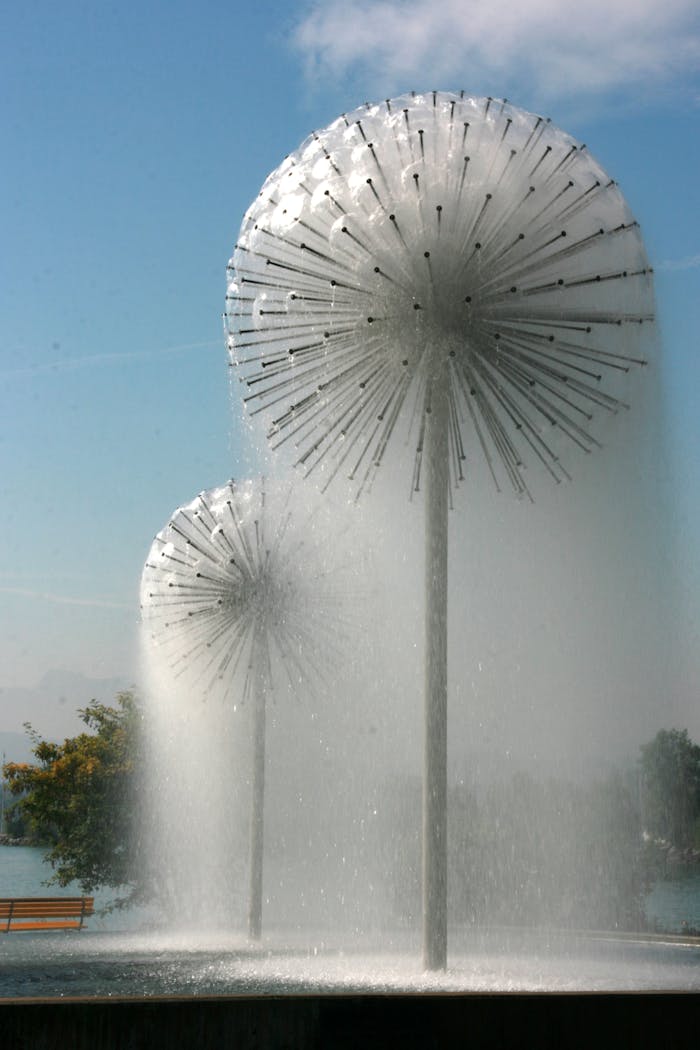 Services Mesmerizing low angle shot of artistic dandelion-shaped water fountains against a blue sky.